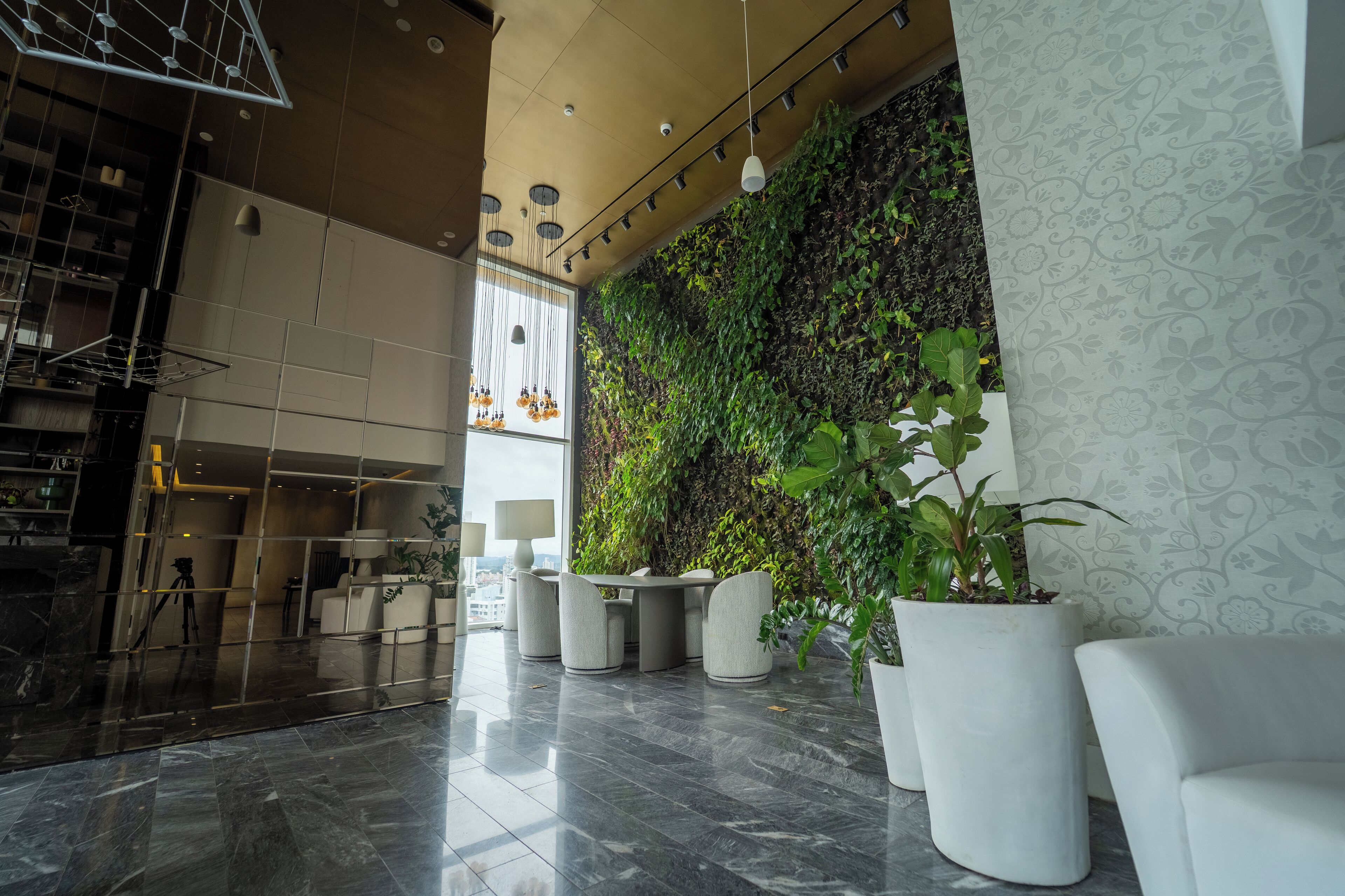 Un vestíbulo moderno con piso de mármol, una zona de estar con mesa y sillas, un jardín vertical verde y una pared con diseño.
