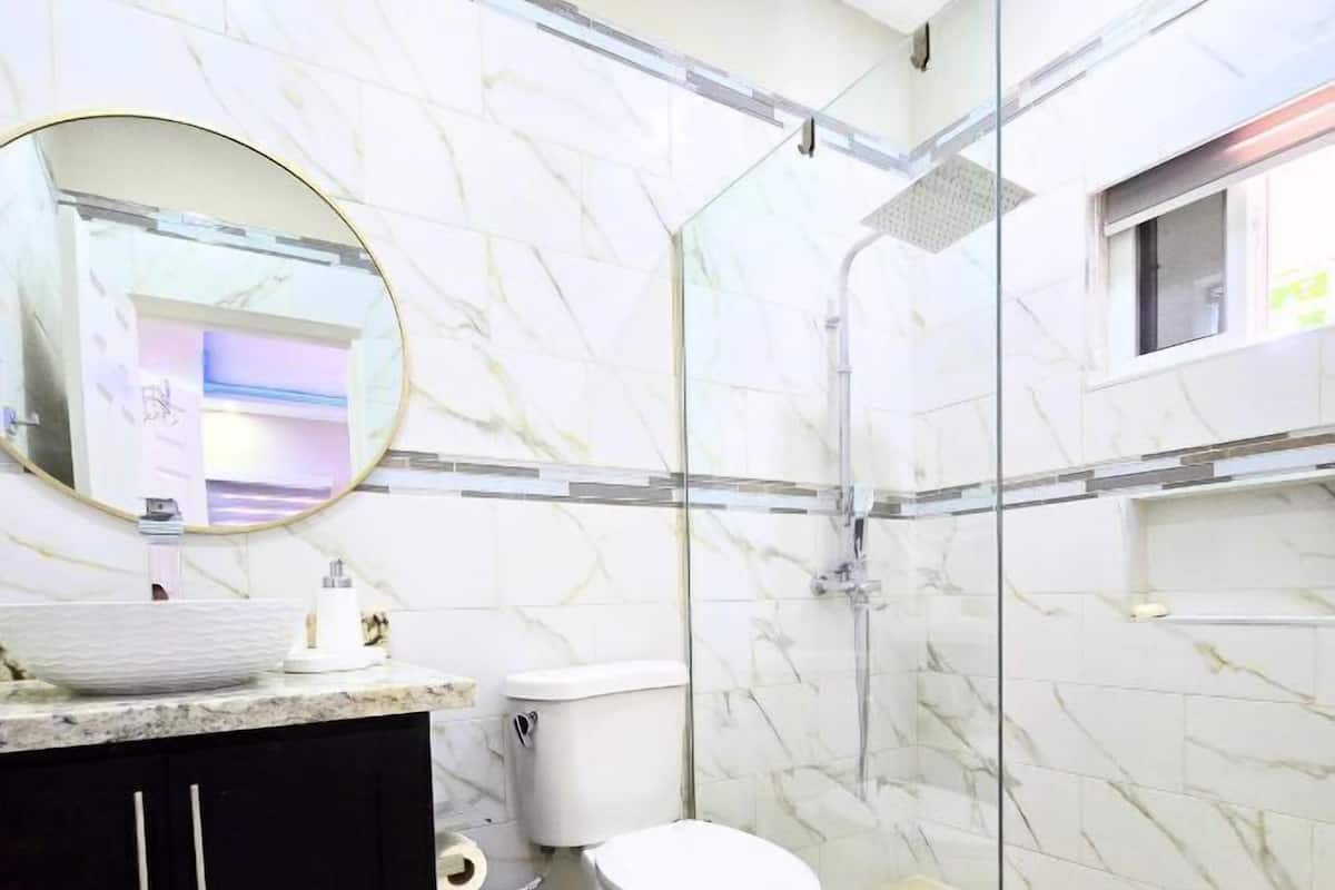 A modern bathroom with a marble backsplash, a white toilet, a black cabinet, and a glass-enclosed shower area.
