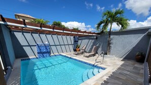 A swimming pool with tiled edges, a sun terrace with lounge chairs, and a palm tree. - Amber Glades (Kingston)