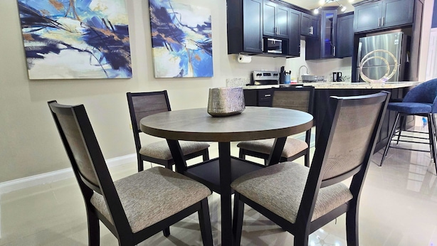 A modern kitchen with dark cabinetry, a central island, and abstract paintings on the wall. - Amber Glades (Kingston)