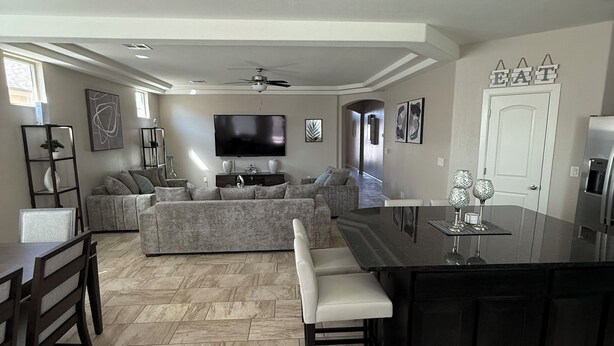A spacious living area with a large sofa, a dining table with chairs, a kitchen island, and a flat-screen TV mounted on the wall. - Westside spot near the Outlet Mall and Providence Hospital, with easy I-10 acces (El Paso)