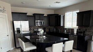A modern kitchen with dark cabinetry, a central island with bar stools, a stainless steel refrigerator, and a microwave. - Westside spot near the Outlet Mall and Providence Hospital, with easy I-10 acces (El Paso)