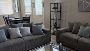 A modern living room with two grey sofas, a glass coffee table, and a dining area with a table and chairs. - Westside spot near the Outlet Mall and Providence Hospital, with easy I-10 acces (El Paso)