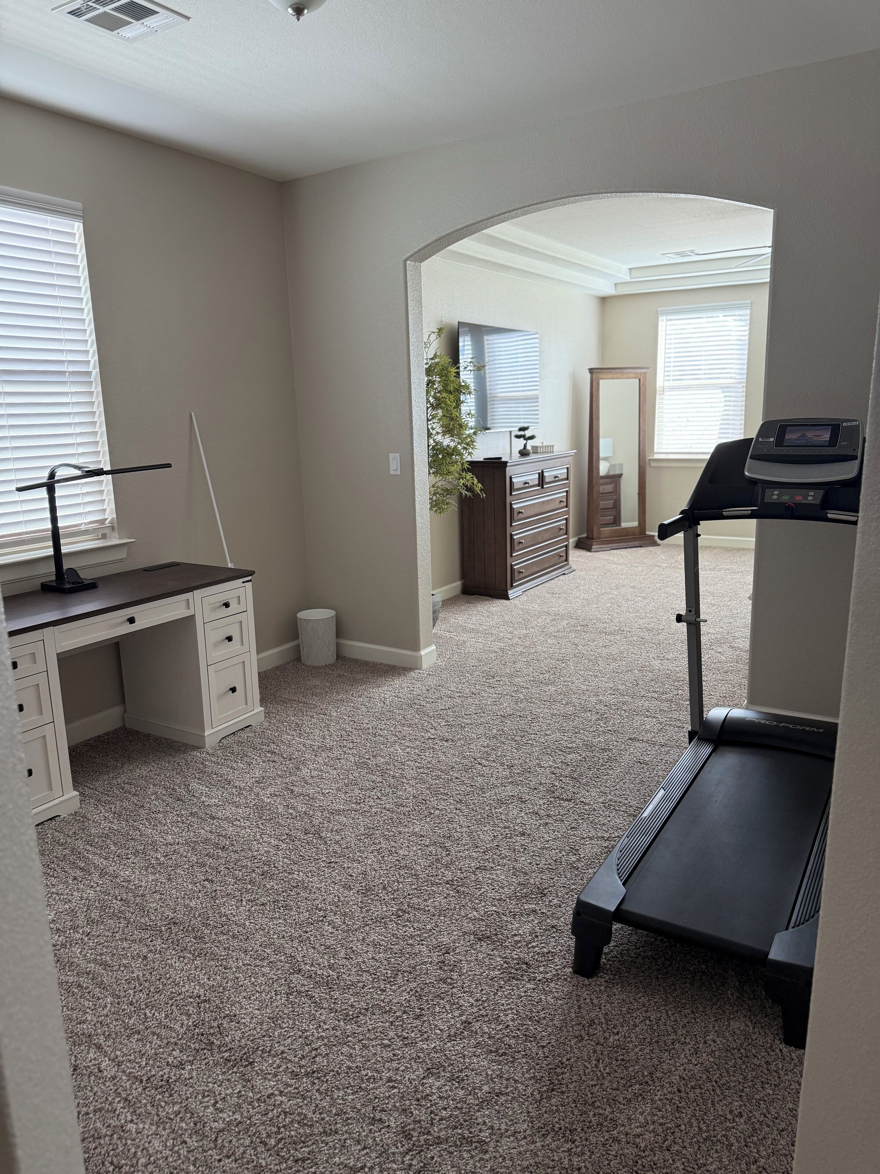 A home office with a desk, chair, treadmill, and a mirror.