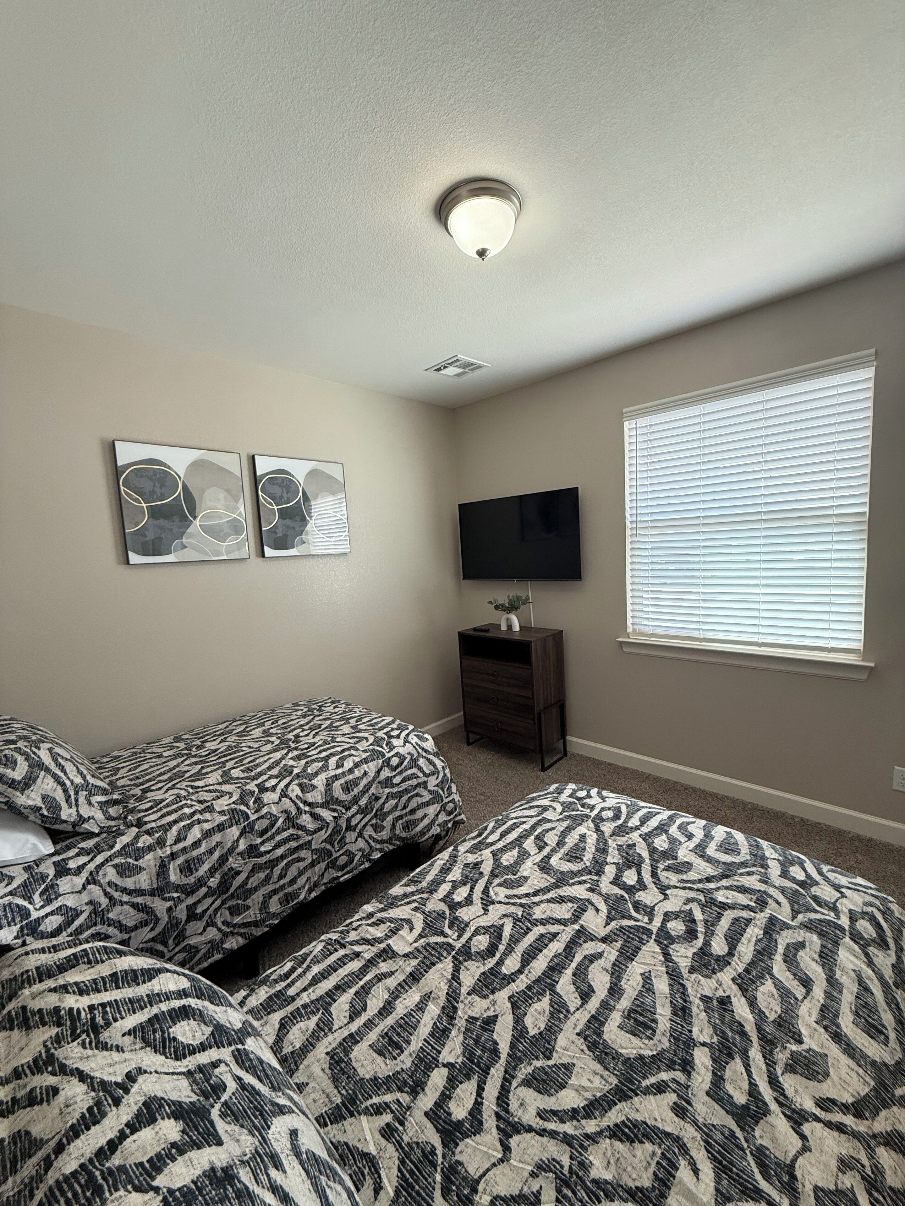 A bedroom with two beds, a TV, and a window with blinds.