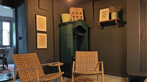 Une pièce comprenant deux fauteuils en osier, une armoire verte et, au mur, des illustrations botaniques encadrées.