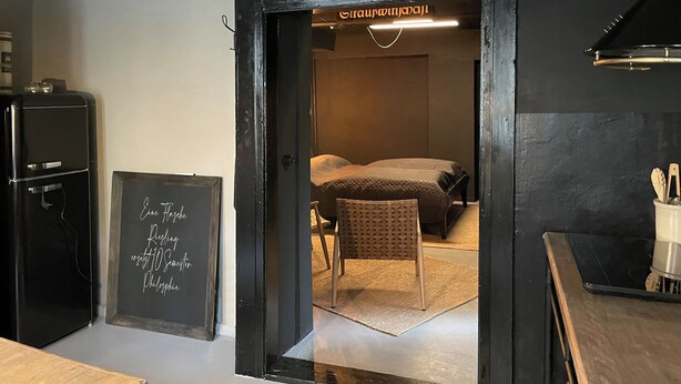 Une pièce comprenant un lit, une chaise, un tableau noir avec du texte, un réfrigérateur et une table en bois.