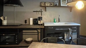 Une cuisine compacte équipée d’un four à micro-ondes, d’une machine à café et d’un évier. On trouve un bol sur le comptoir et une chaise devant la table.
