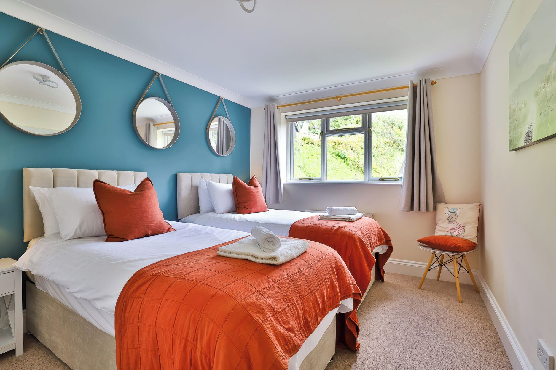 A double room with two beds, a window with curtains, and a small table with a chair.