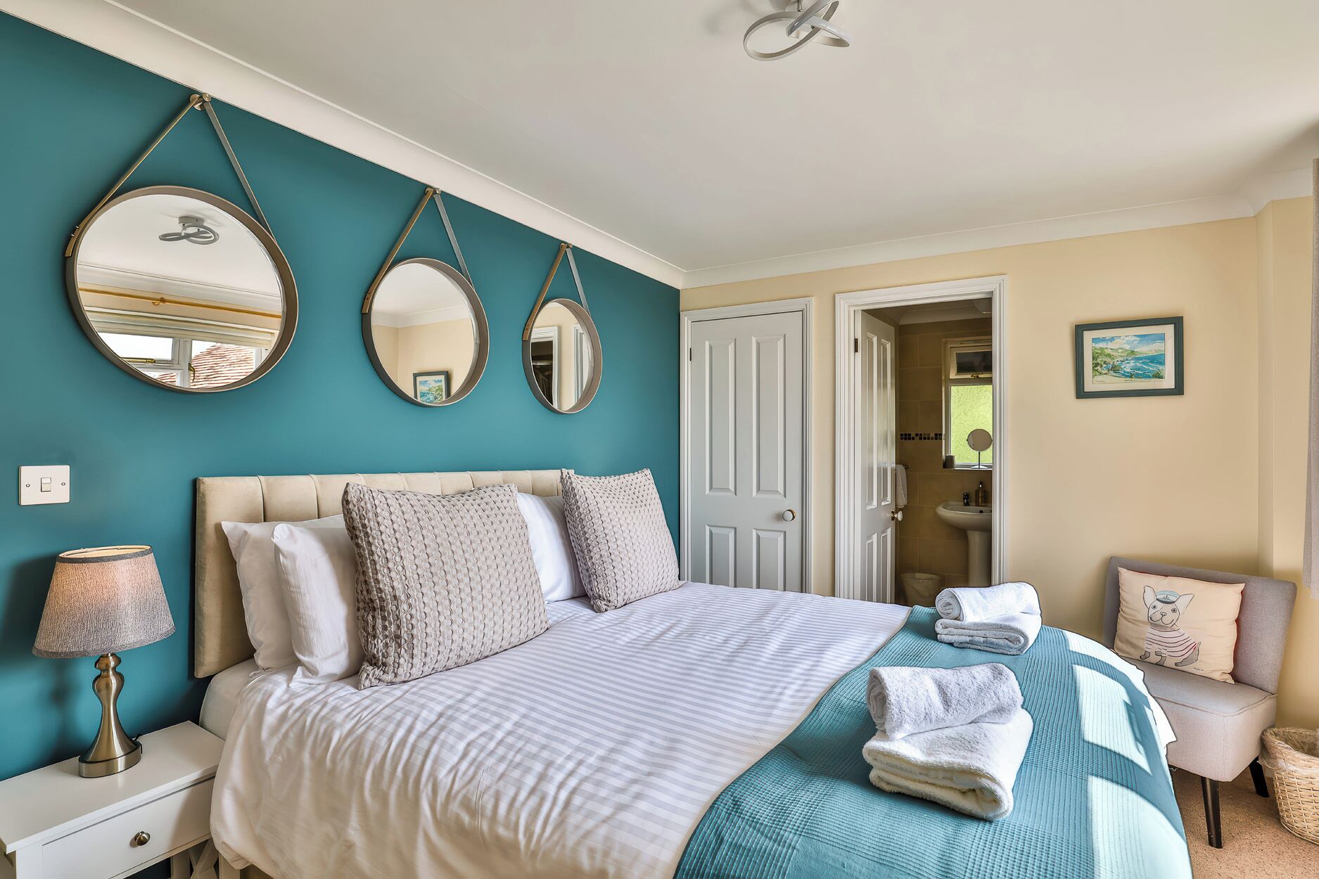 A bedroom with a bed, two wall mirrors, a bedside lamp, a door, and a view of the bathroom.