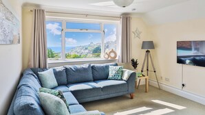 A living room with a large window, a sofa, a floor lamp, and a TV. - Beer View Cottage (Seaton)