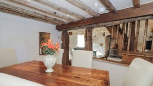 Une table à manger en bois, entourée de chaises blanches, un vase rempli de fleurs et un intérieur rustique avec des poutres apparentes et un mur en pierre.