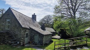Une maison en pierre avec un toit en pente, une cheminée et un petit porche avec des marches menant à l’entrée.