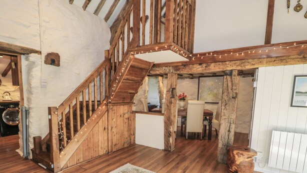 Un intérieur rustique avec un escalier en bois, un coin repas et une cuisine visible au fond.