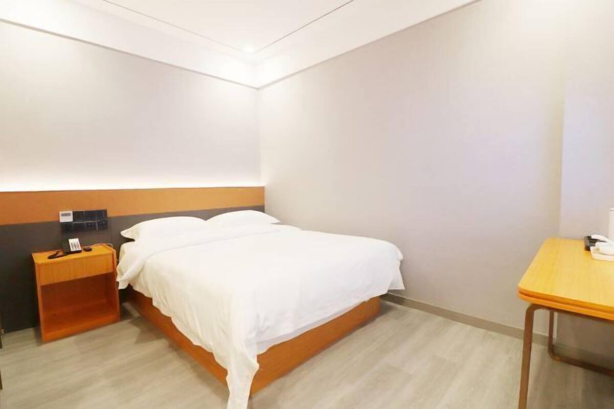 A hotel room with a single bed, a wooden nightstand, a small table, and a wall-mounted charging station.