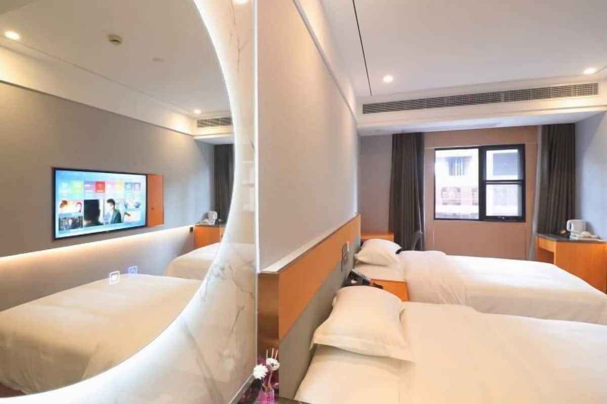 A hotel room with two beds, a TV on the wall, and a window with curtains.