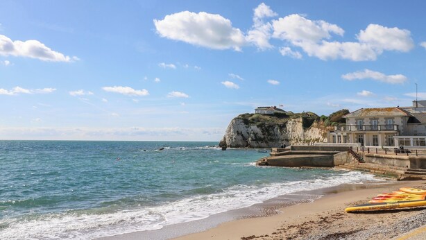 Un paysage côtier avec une plage de sable, une falaise rocheuse et un bâtiment sur lequel flotte un drapeau.
