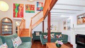 Un salon spacieux avec un escalier en bois, des canapés verts, une table basse en bois et une cheminée.