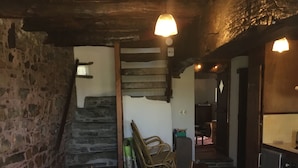 Ein rustikaler Essbereich mit einem langen Holztisch, Stühlen und einer gemusterten Tischdecke.