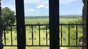 Ein Balkon mit schmiedeeisernen Geländern, der auf eine ländliche Landschaft mit Feldern und Bäumen blickt.