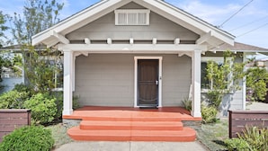A two-story house with a front porch, a door with a metal gate, and a small window above the door. - Mins to Belmont Shore - Firepit - Game Room - BBQ - Free Parking - FIFA 2026! (Long Beach)