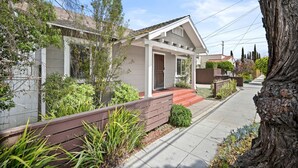 A residential house with a front porch, a red door, and a small front yard with plants and a wooden bench. - Mins to Belmont Shore - Firepit - Game Room - BBQ - Free Parking - FIFA 2026! (Long Beach)