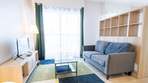 A modern living room with a grey sofa, a glass coffee table, a TV on a wooden stand, and a built-in wooden shelving unit. - Le Tribut - with car park (Tours)