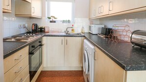 Una cocina compacta con un lavamanos, estufa, horno y microondas. Hay una ventana con vistas al exterior, y armarios con pomos.