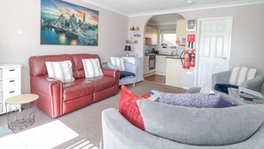Un salón con un sofá de cuero rojo, un sillón gris y un cuadro de un paisaje urbano.