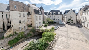 Une place historique, bordée de bâtiments en pierre, avec un petit pont et une zone pavée.