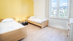 Une chambre avec deux lits, une fenêtre donnant sur la ville et une table de chevet avec des lampes.