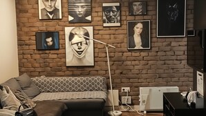 Una sala de estar moderna con pared de ladrillo, piso de madera y sofá modular. Se observan varias obras de arte enmarcadas en la pared y una lámpara de pie blanca.