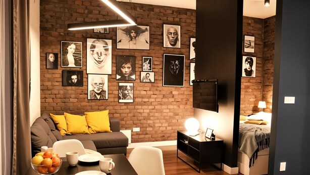 Una sala moderna con pared de ladrillo, un sofá con cojines amarillos, una mesa de comedor con un tazón de fruta y un televisor montado en la pared.