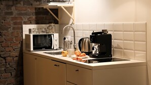 Cocina con microondas, hervidor y lavabo. Hay frutas y un plato en la encimera.