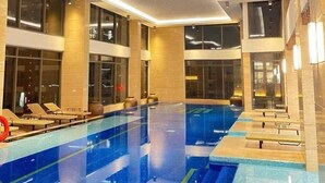 Una piscina interior moderna con varias pistas de natación, sillas de descanso y un techo alto con iluminación empotrada.