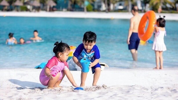 Niños jugando en una playa arenosa con una piscina al fondo.