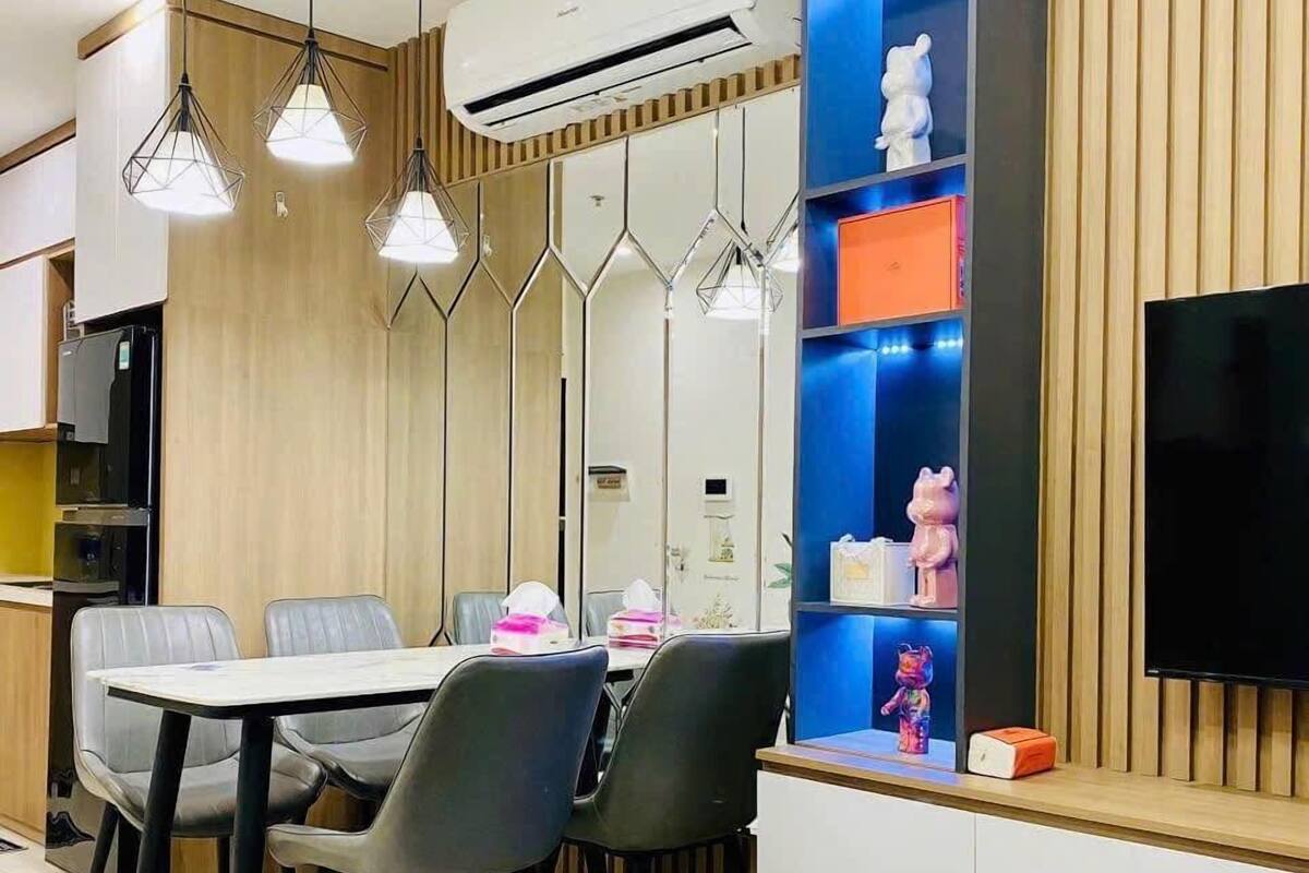 A modern living room with a dining area, featuring a flat-screen TV, pendant lights, and a built-in shelf with decorative items.