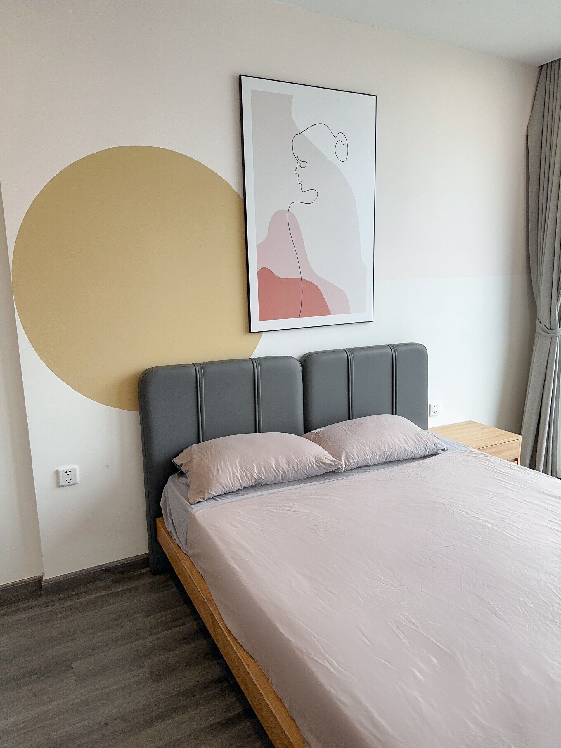 A bedroom with a bed, a headboard, a wall-mounted artwork, and a large circular design on the wall.