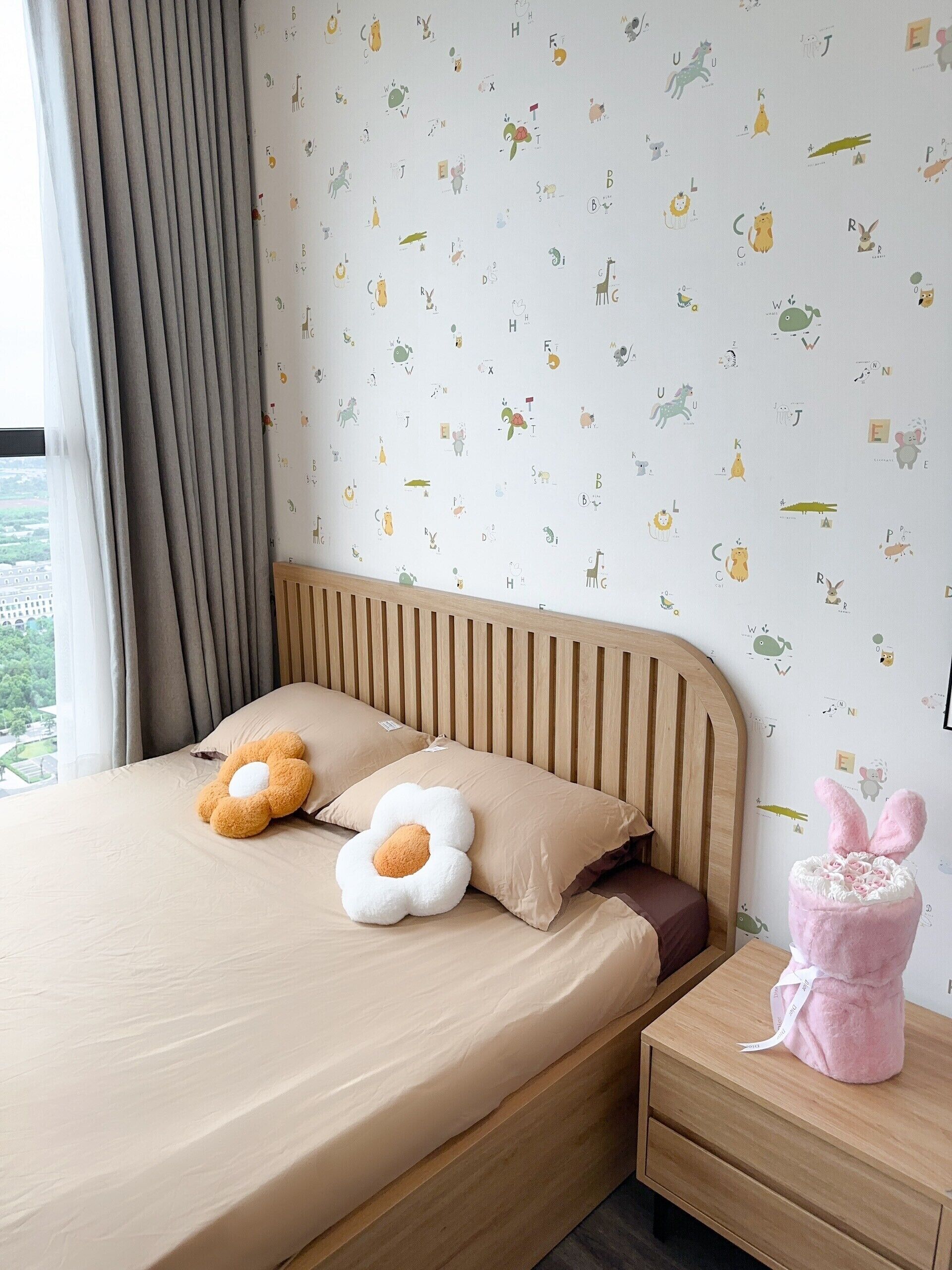 A bedroom with a bed, pillows, a nightstand, and a wall with alphabet and animal decals.