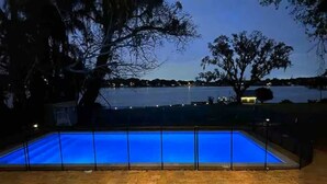 Piscina rectangular de color azul, rodeada por una terraza de madera y una valla metálica.