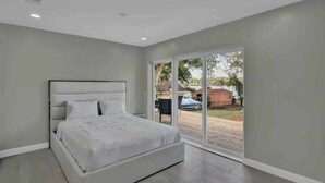 Un dormitorio moderno con una cama grande, un ventanal corredero que da a una terraza y vistas al exterior.