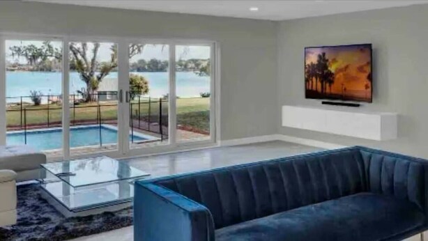 Un moderno salón con un sofá azul, una mesa de centro de cristal y vistas a una piscina a través de amplios ventanales correderas.
