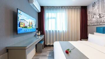 A hotel room with a bed, a desk with a flat-screen TV, a window with curtains, and a wall with a cityscape mural.