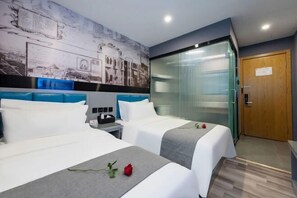 Habitación de hotel con dos camas, una mesita de noche, un muro con un mural de paisaje urbano, una puerta de cristal y una puerta de madera.