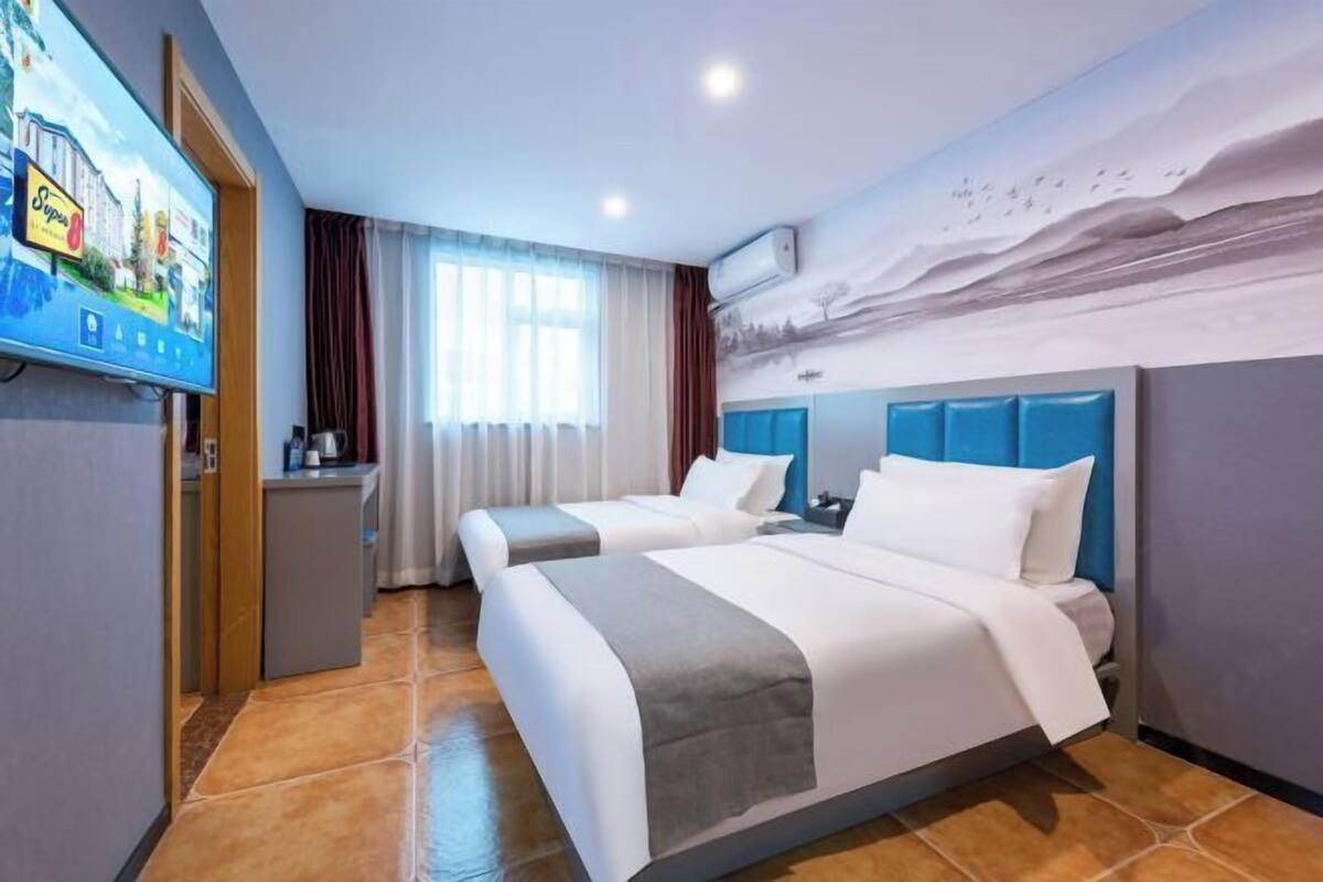 Quarto de hotel com duas camas, televisão, escrivaninha e um mural na parede.