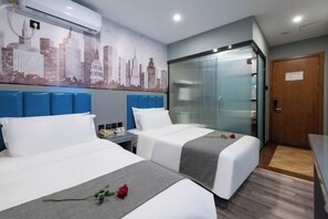 Habitación de hotel con dos camas, un mural de paisaje urbano, una pared de vidrio y una puerta de madera.