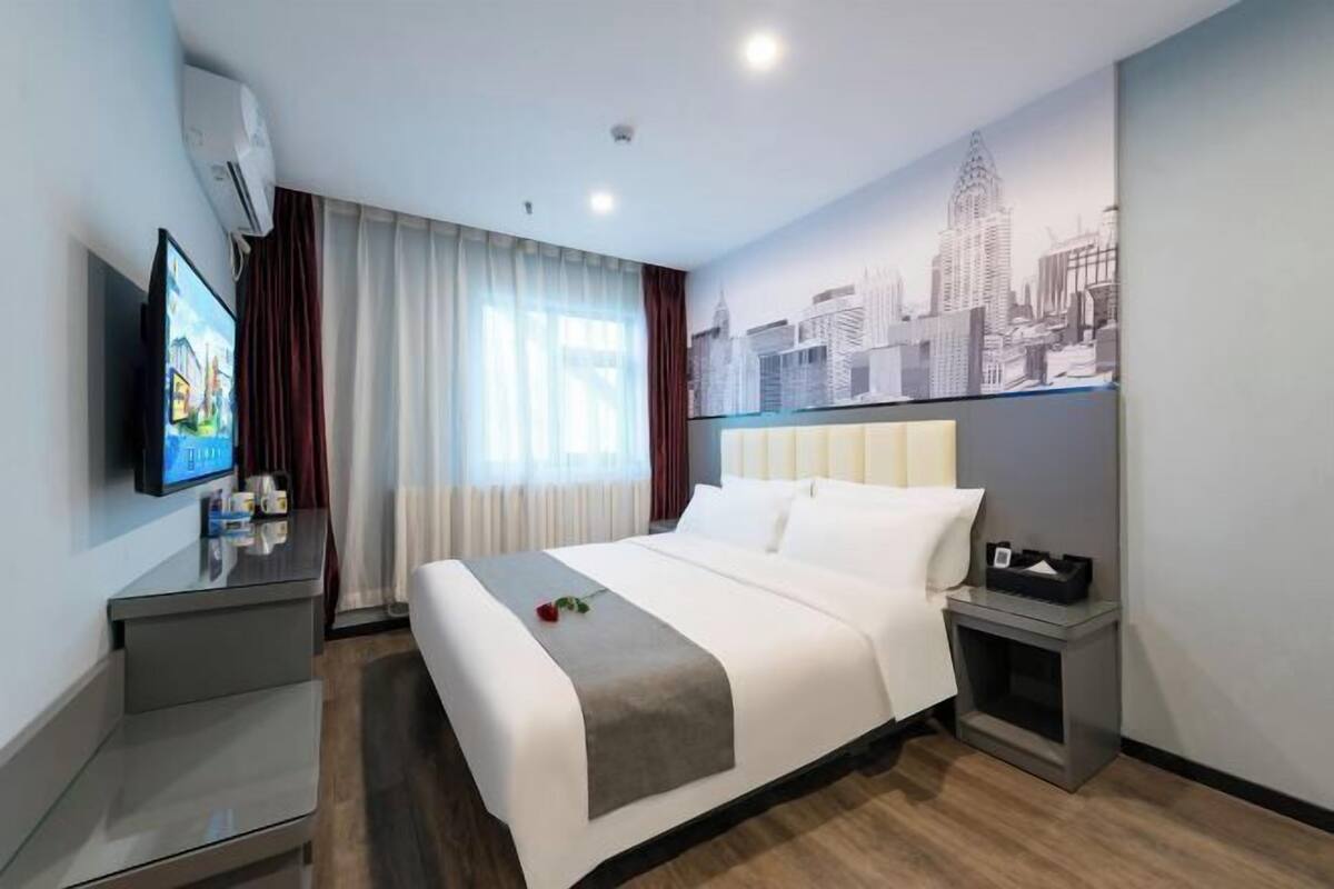 Quarto de hotel com cama, televisão, mural de paisagem urbana e mesa de cabeceira.