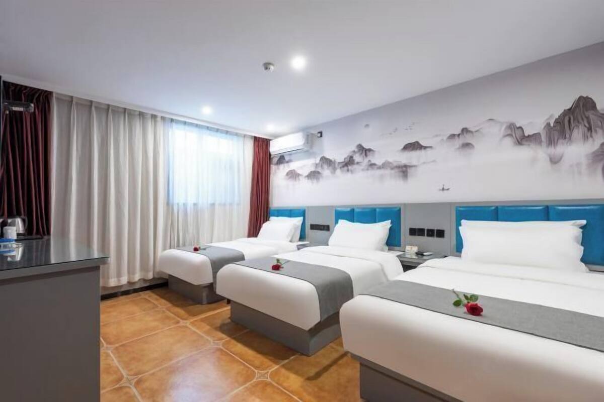 Quarto de hotel com duas camas, uma escrivaninha e um mural de montanhas.