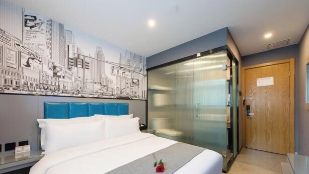 A hotel room with a bed, a cityscape mural, a glass partition, and a wooden door. - Super 8 (Beijing West Gongyi Bridge) (Beijing)