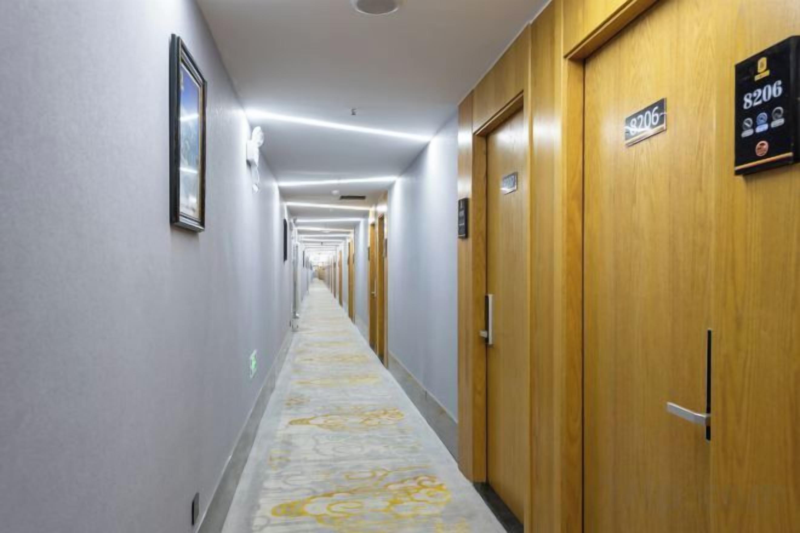 Un couloir d’hôtel avec des portes portant les numéros des chambres, un sol recouvert de moquette et un mur de couleur claire.
